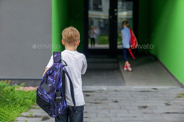 Small students, boy and girl, approach to door of school. Arriving at school gates. Back to school