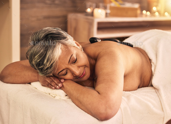 Woman, spa and relax with stone massage on back for skincare treatment, holistic therapy and beauty