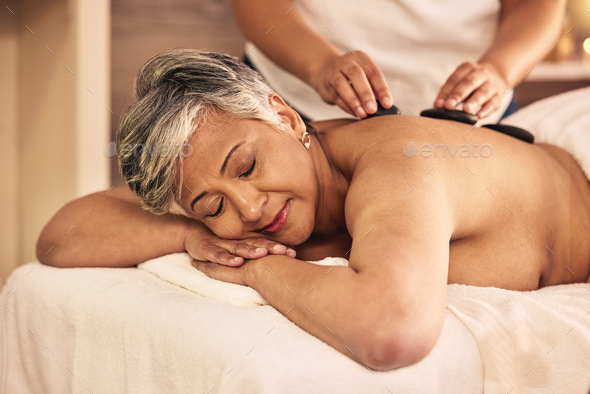 Woman, spa and stone massage on back for skincare treatment, holistic therapy and stress relief at