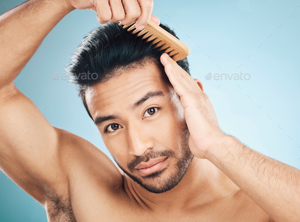 Portrait, beauty and a man brushing his hair on a blue background in studio for self grooming. Face