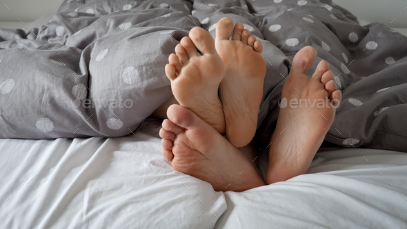 Couple\'s feet lying and hiding under the blanket on a cozy bed. Concept of family conflict