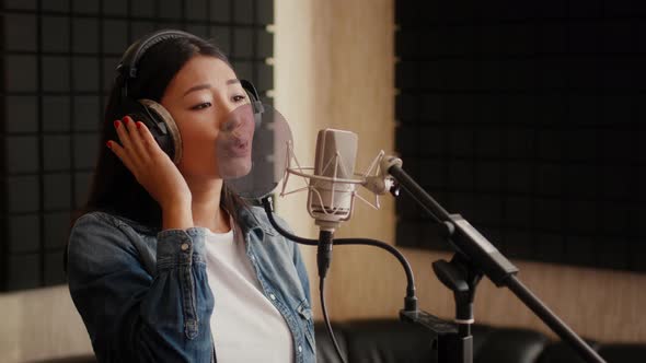 Talented Asian Female Singer Wearing Headphones Singing Song To Mic In Studio alt
