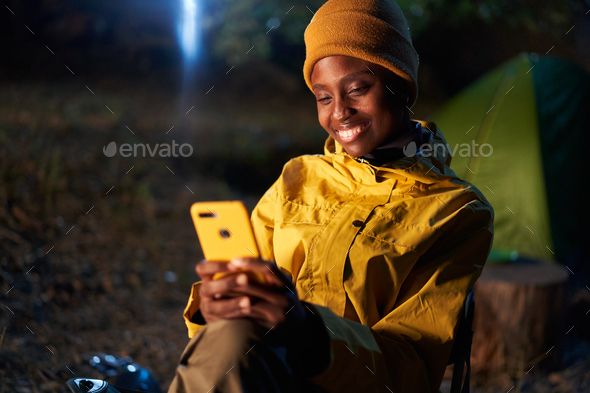 Young African girl using her cell phone and sitting camping on a winter day at night.