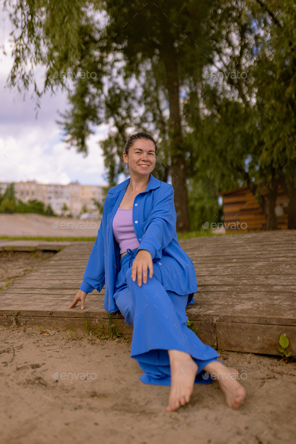happy woman in wrinkle-free travel clothes sitting on wooden embankment. summer weekend outdoors