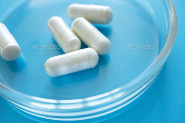 Probiotic supplement in capsules in glass petri dish on blue background