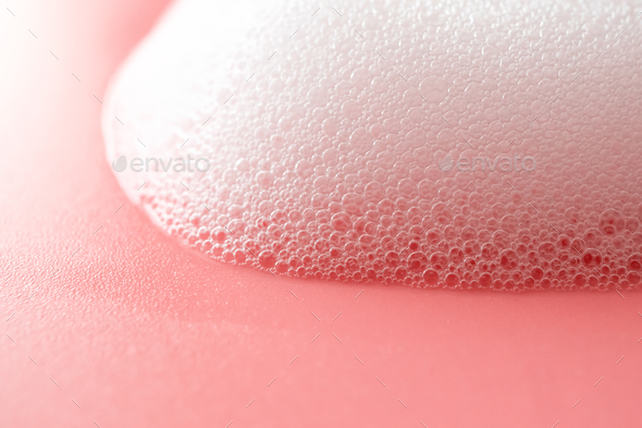 White foam from soap, shampoo or cleanser on pink background