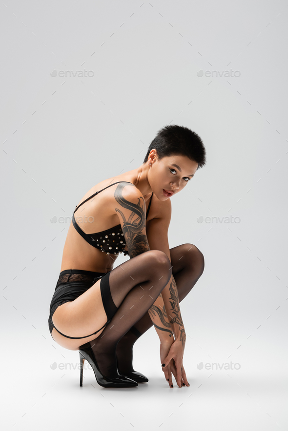 full length of provocative and sexy woman with tattooed body and short  brunette hair wearing bra Stock Photo by LightFieldStudios