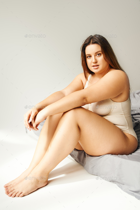 brunette woman with natural makeup and plus size body wearing beige  bodysuit and posing Stock Photo by LightFieldStudios