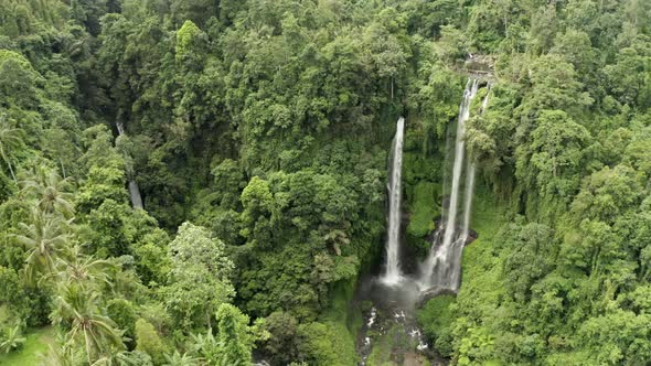 Slow drawing back tracking shot of tall lush jungle waterfall alt