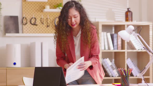 Business woman standing in front of laptop in home office showing paper sheet to customer have graph alt