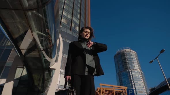 A Girl with a Leather Briefcase in Her Hands Stands Near a High Office Building