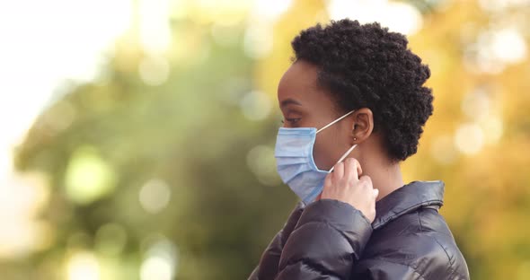 Portrait of African Woman Standing Sideways To Camera Outdoors in Autumn Weather Putting on Medical alt