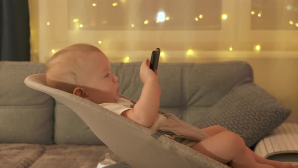 Baby Boy Sitting on Rocking Chair for Babies Playing with Smartphone Cute Toddler Watching Cartoon alt