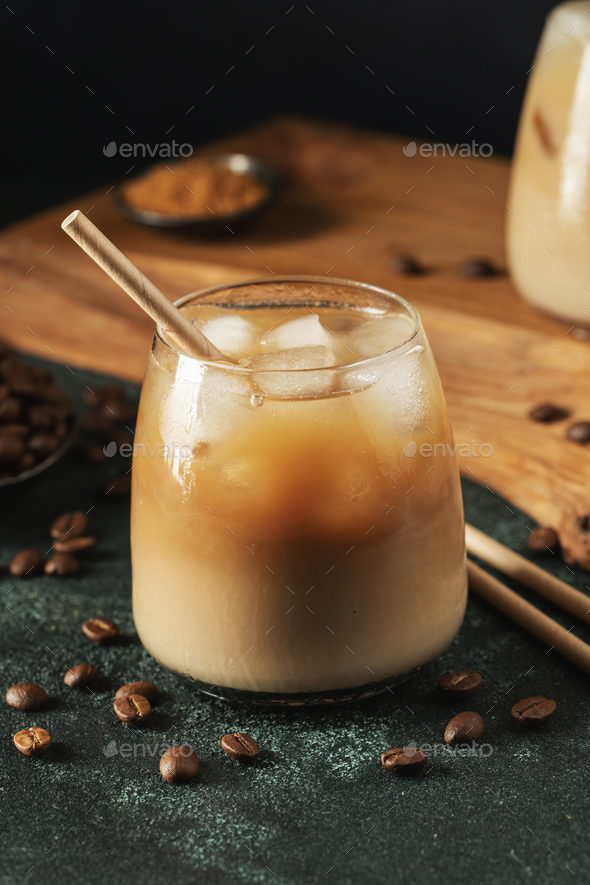 Ice coffee in a glass with cream poured over and coffee beans