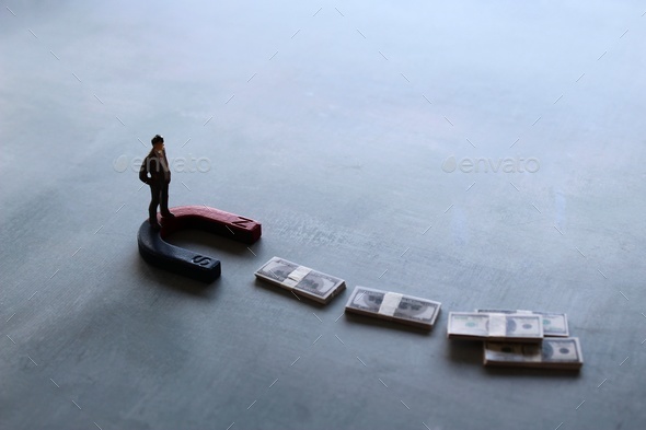 Selective focus image of miniature businessman attracts money using magnet
