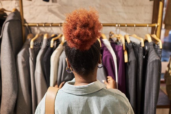 Back view black young woman browsing clothes on racks in clothing store