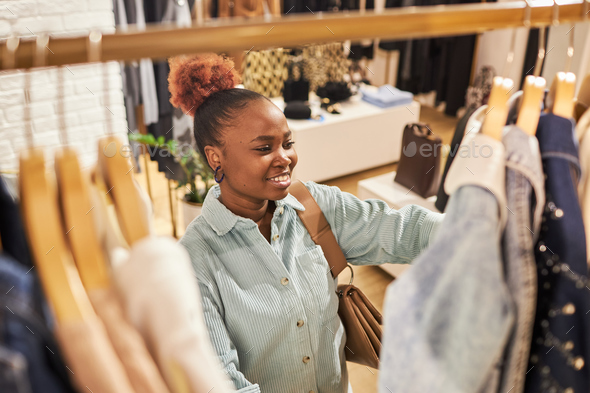 Smiling black woman browsing clothes on rack in clothing store
