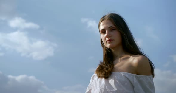 Carefree Young Woman Is Flirting with Camera, Portrait Against Blue Cloudy Sky alt