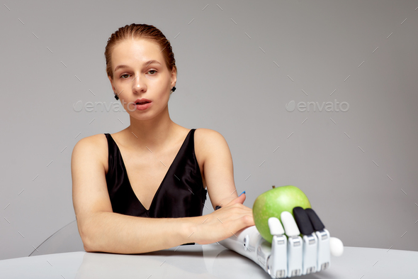 Young charming girl with disability wearing sensory bionic prosthetic arm seats at the table