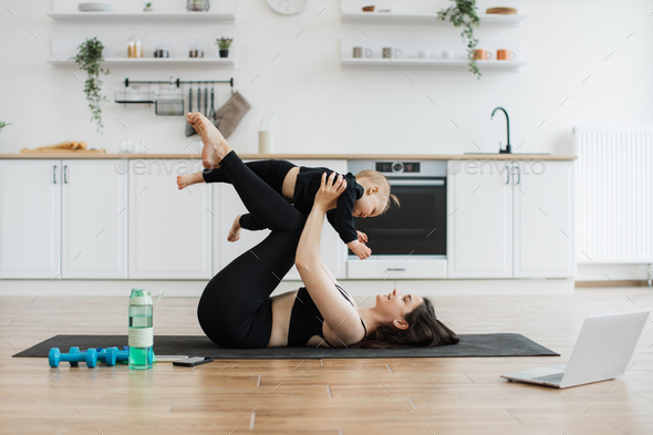 Mother carrying infant on bent knees while lying on yoga mat
