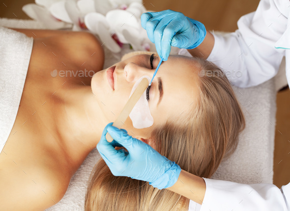 Young woman undergoing procedure of eyelashes lamination in beauty salon
