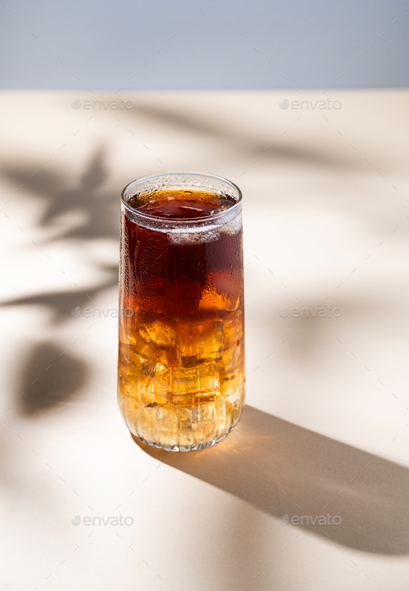 Long Island iced tea cocktail with hard liquor with rum, cola, lemon and ice on yellow background
