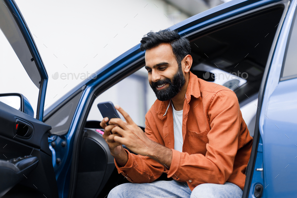Eastern Man Using Phone Sitting In Auto With Opened Door