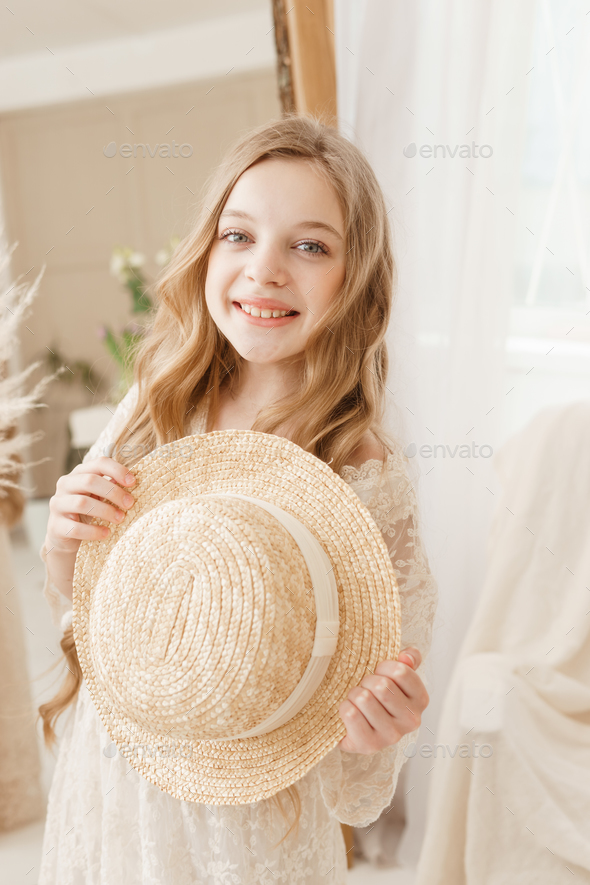 A beautiful teenage girl with long hair measures a straw hat in front of a mirror. Self-admiration