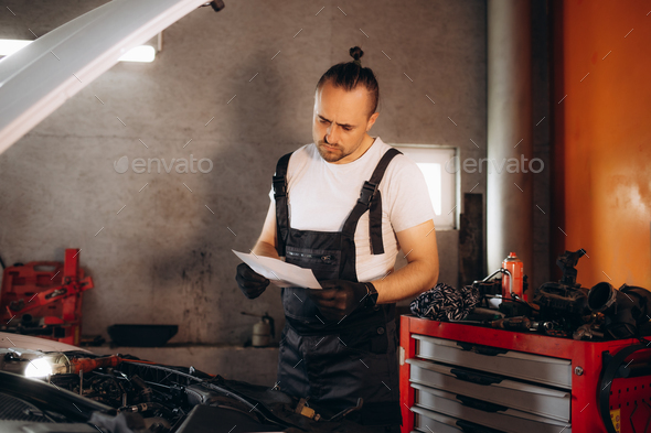 Auto mechanic examining paperwork and communicating over mobile phone in a repair shop.