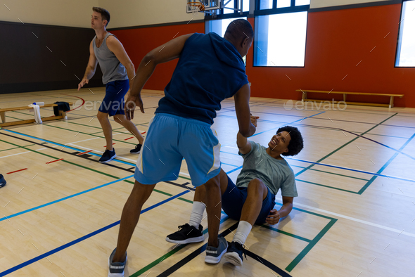 Diverse male basketball players helping to get up at gym