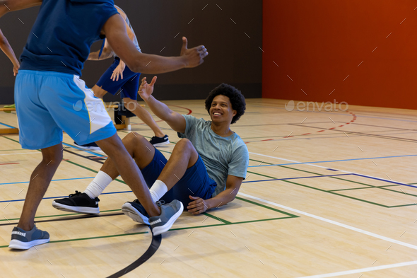 Diverse male basketball players helping to get up at gym, copy space