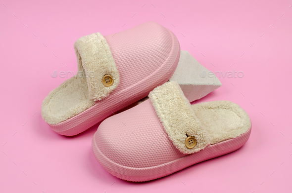 Warm indoor slippers with fur on a podium made of natural stone, pink background