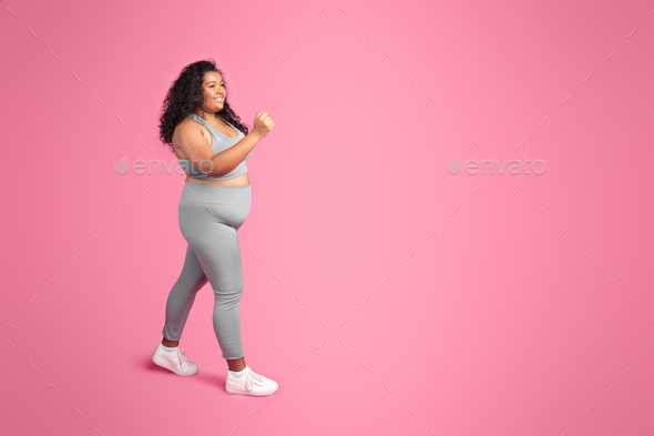 Glad black oversize woman in sportswear training, enjoying jogging and workout,  pink background Stock Photo by Prostock-studio