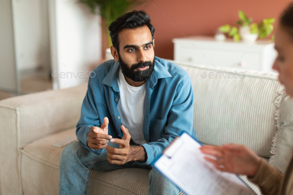 Young Indian man consulting with professional psychologist sitting indoor
