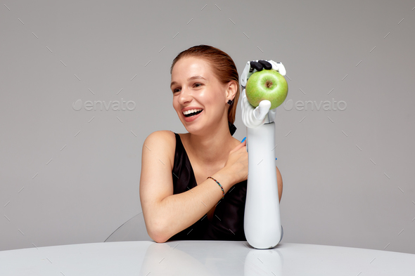 Young smiling girl with disability wearing sensory bionic prosthetic arm seats at the table
