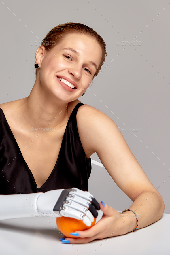 Young charming girl with disability wearing sensory bionic prosthetic arm seats at the table