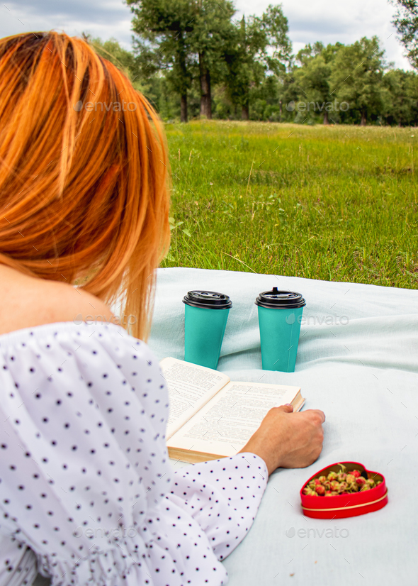 young woman reading a book at a summer picnic, in a public park, girl with red hair at a picnic, pi