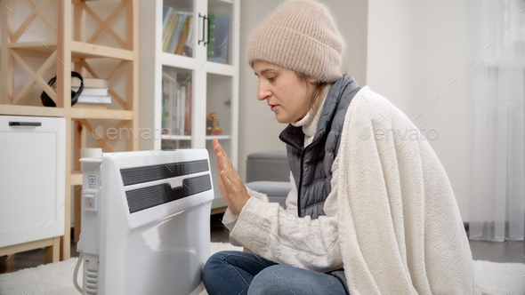 Young woman freezing in cold house warming at electric radiator.Concept of energy crisis, high bills