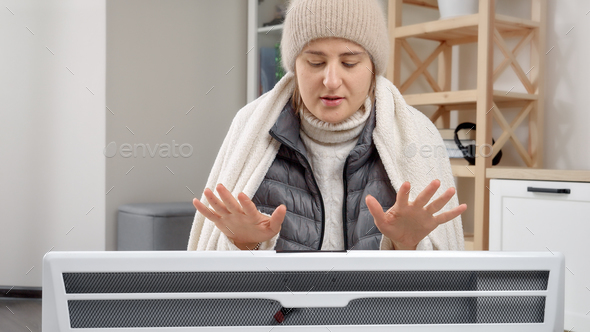 Woman freezing in her house warming at the electric heater. Concept of energy crisis, high bills