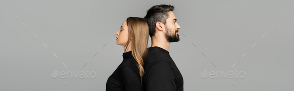 Side view of relaxed and bearded man in black t-shirt standing back to back with fair haired wife