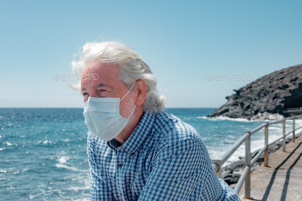 Portrait of handsome white-haired senior man wearing mask enjoying summer and nature at sea