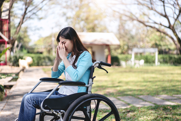 Young asian woman on wheelchair in the garden and touching hands to rubbing nose while stressed
