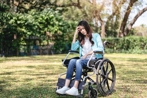 Young asian woman on wheelchair in the garden and touching hands to rubbing nose feeling stressed