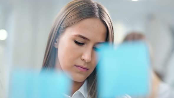 Confident Young Business Woman Stick Colored Sticky Notes on Glass Board Looking and Brainstorming alt