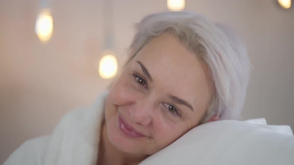 Closeup Front View Positive Mature Woman Smelling Fresh Clean Laundry Smiling Looking at Camera alt