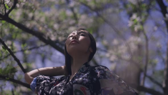 Beautiful Asian Woman Dancing in Spring Blooming Sakura Garden in Sunlight alt