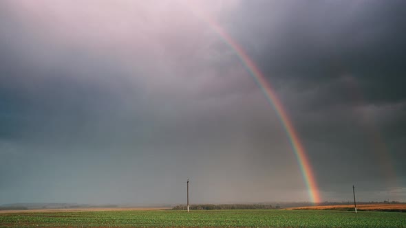 Dramatic Sky During Rain With Rainbow On Horizon Above Rural Landscape Field alt