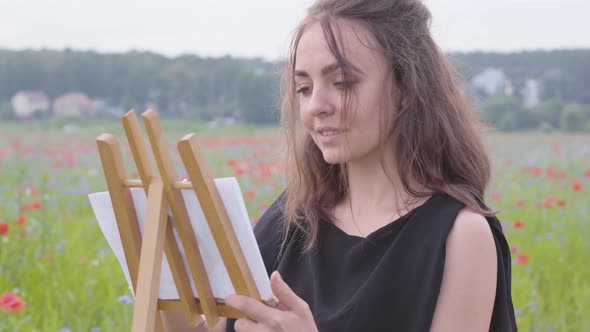 Portrait of Cute Smilling Girl Painting on the Easel Tanding on the Poppy Field. Young Woman Artist alt