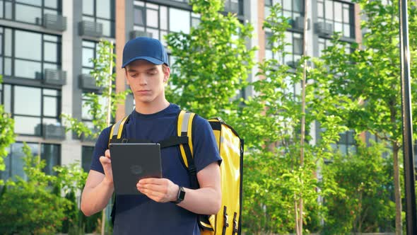 Portrait Young Man Courier Food Delivery with Thermal Backpack Uses Tablet alt
