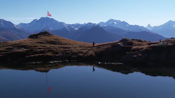 Aerial dolly left in stunning mountain and lake panorama with a solo backpacker alt